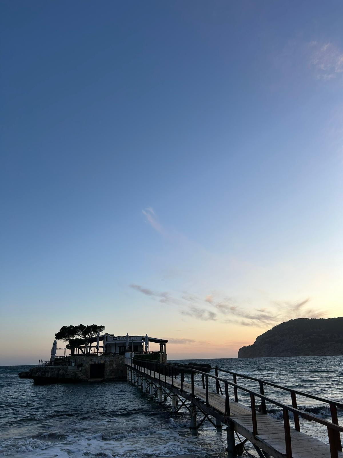 Restaurante Illeta Mallorca: eten op een rotseilandje bij Camp de Mar 3 Het rotseilandje met Restaurante Illeta vanaf de zijkant gezien, met golven tegen de pijlers van de loopbrug en de landtong erachter