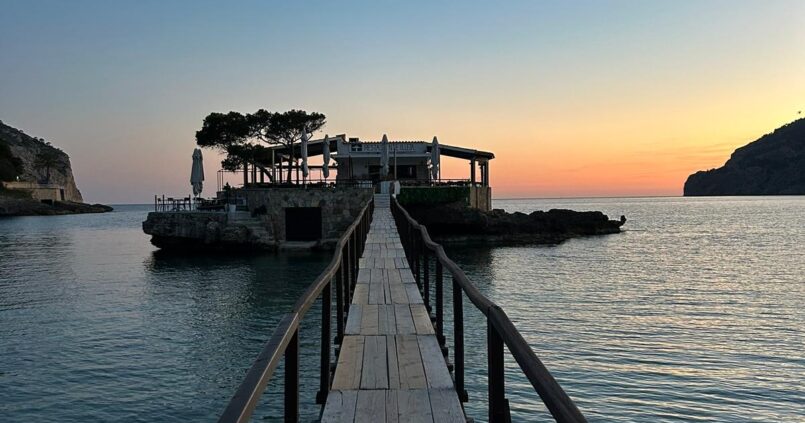 De houten loopbrug naar het rotseilandje met Restaurante Illeta bij Camp de Mar, in de schemering met de naam op de gevel