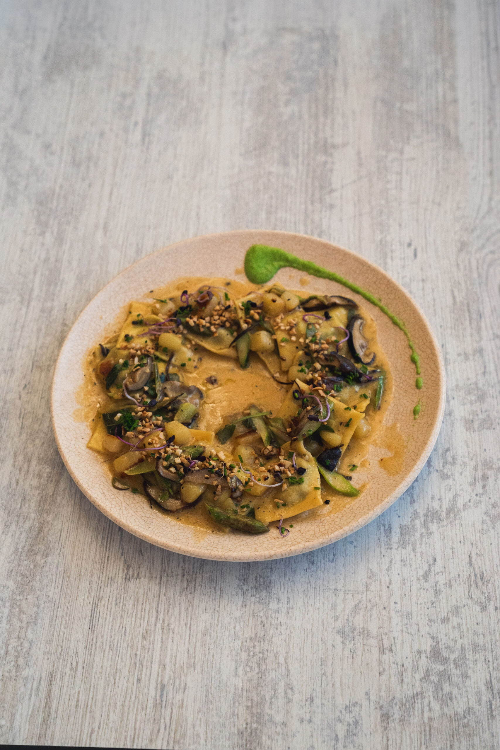 Verse ravioli in een romige saus met asperges, shiitake en gehakte amandel, in een kring op een beige bord