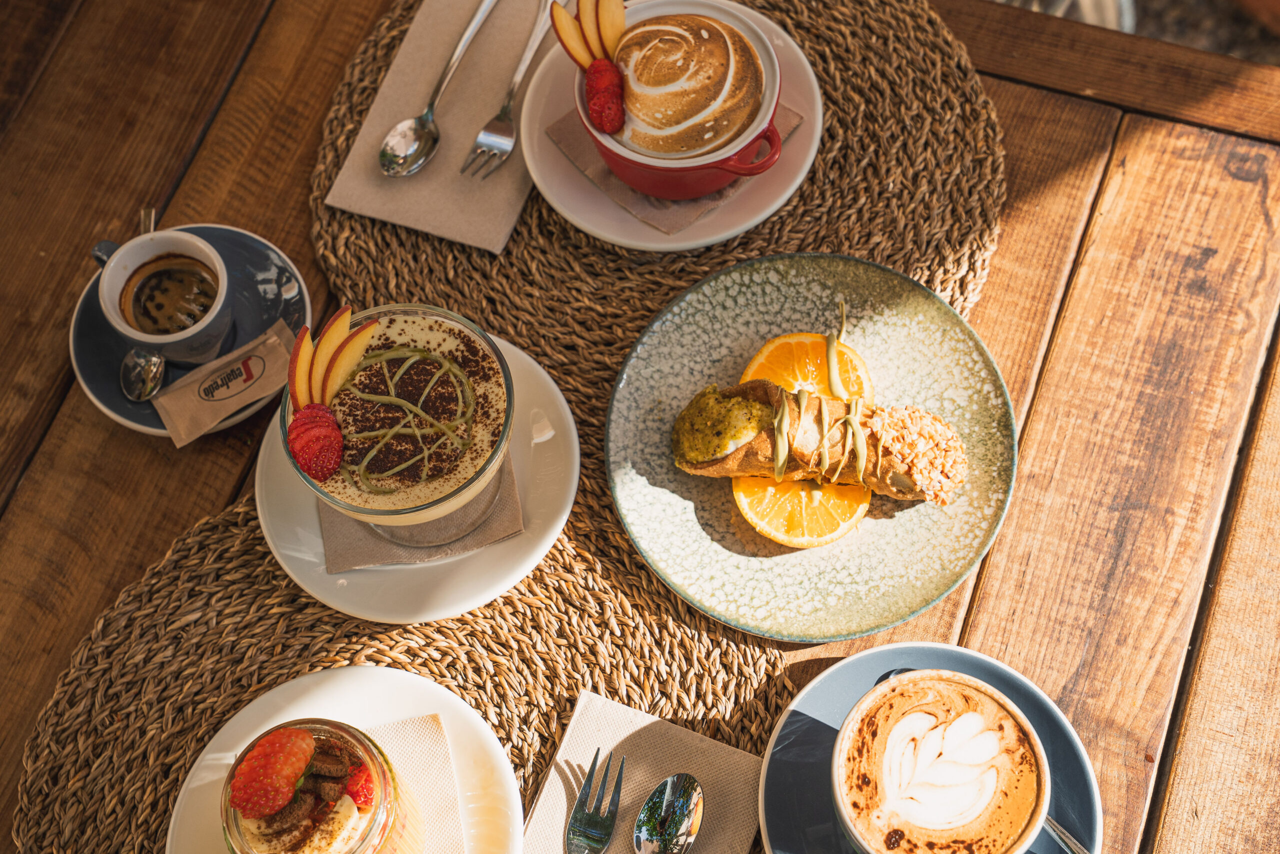Huisgemaakte toetjes van Sa Font Fresca op een houten tafel: tiramisu in een glas, een cannolo siciliano met sinaasappel, een lemon pie in een rood potje en twee cappuccino's