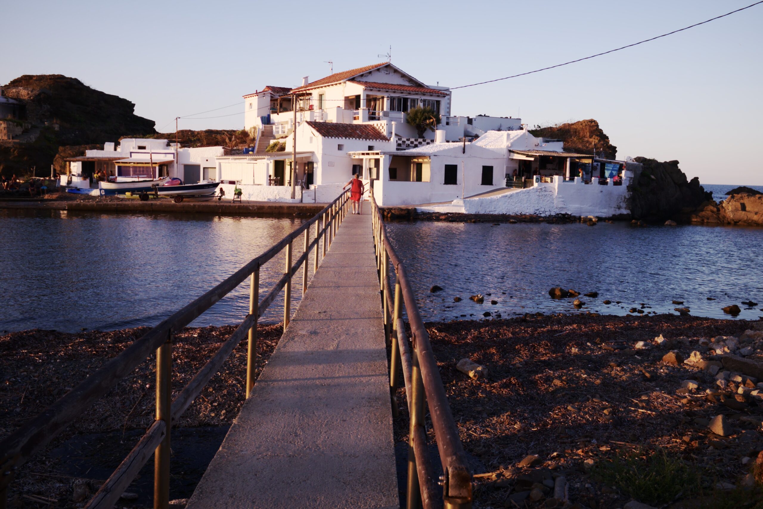 Sa Mesquida Menorca: het dichtstbijzijnde noordkuststrand vanaf Maó 6 Smalle loopbrug naar het rotseilandje sa Bateria Amagada met witte zomerhuisjes bij Sa Mesquida