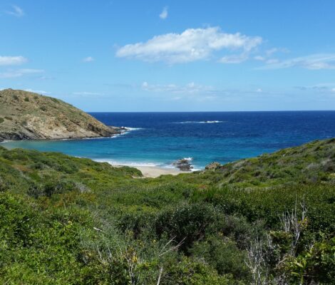 Het zandstrand van Sa Mesquida op Menorca met de rotskop Es Pa Gros en blauw water
