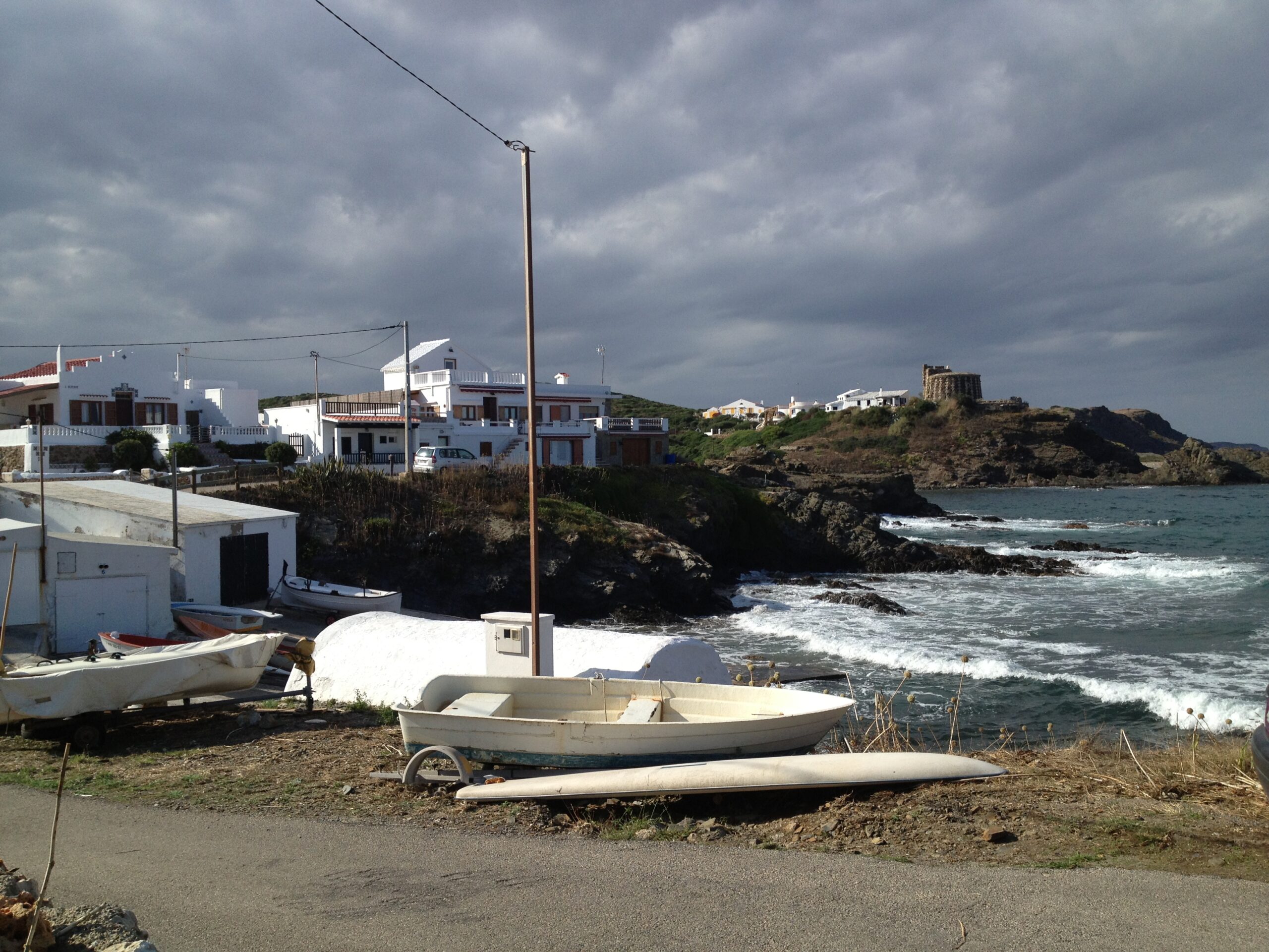 Sa Mesquida Menorca: het dichtstbijzijnde noordkuststrand vanaf Maó 2 Vissersbootjes en witte huizen van het gehucht Sa Mesquida met de verdedigingstoren op de rots en branding op de kust