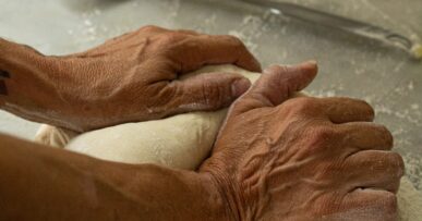 Handen die pizzadeeg kneden op een bebloemd stalen werkblad in de keuken van Sa Panxa op Formentera