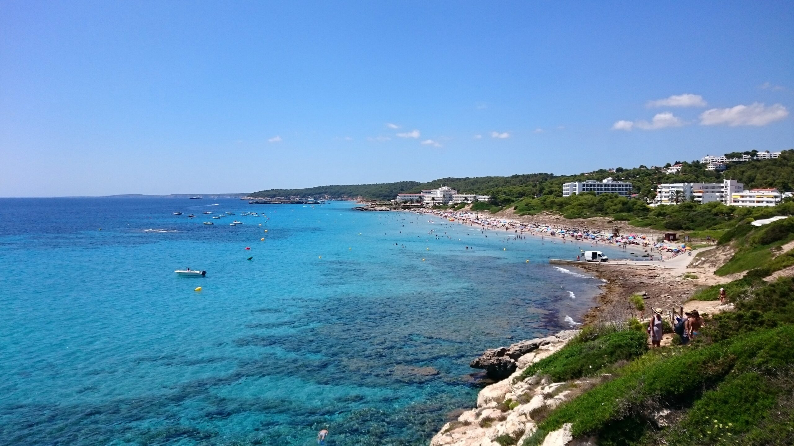 De baai van Santo Tomás op Menorca gezien vanaf de Punta de Talis, met turquoise water en de hotels achter het strand
