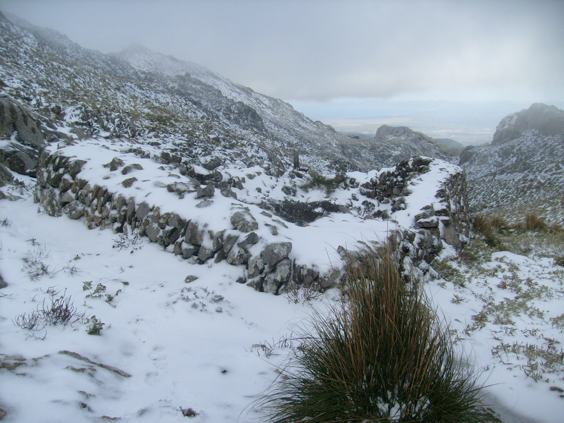 Ronde sneeuwput van losse stenen onder de sneeuw op het Massanella-massief, met in de verte de baai van Alcúdia