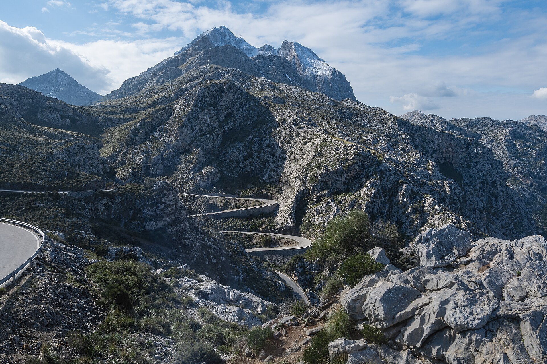 De besneeuwde top van de Puig Major boven kale kalksteenruggen, met de slingerende weg naar Sa Calobra in de diepte
