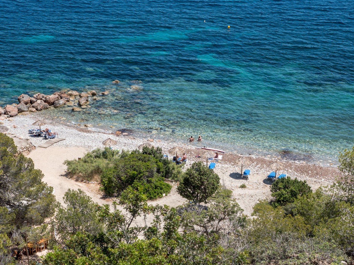 De baai van Ses Boques van bovenaf gezien, met glashelder turquoise water, rieten parasols op de kiezels en pijnbomen tot aan de waterlijn