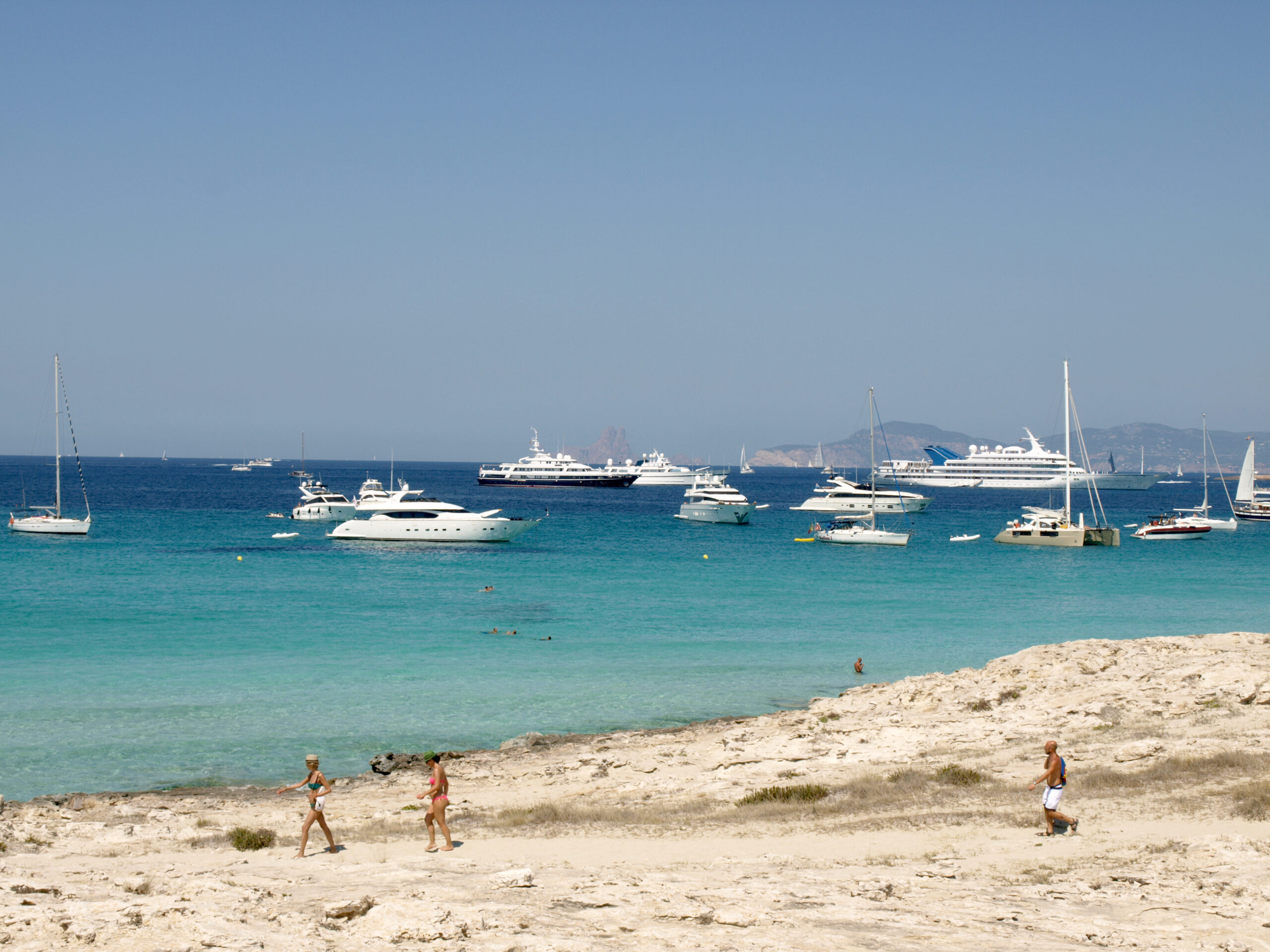 Ses Illetes Formentera: strandgids met de regels van 2026 5 Zeiljachten en motorjachten voor anker in het turquoise water voor Ses Illetes, met de kust van Ibiza aan de horizon