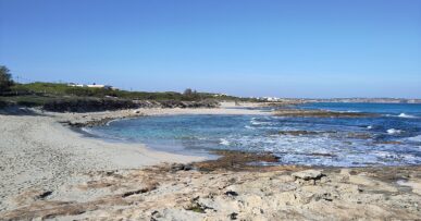 Een van de zandkommen van Ses Platgetes op Formentera, met turquoise water tussen de rotsplaten en duinen erachter