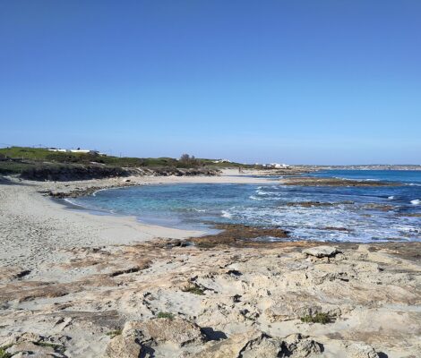 Een van de zandkommen van Ses Platgetes op Formentera, met turquoise water tussen de rotsplaten en duinen erachter