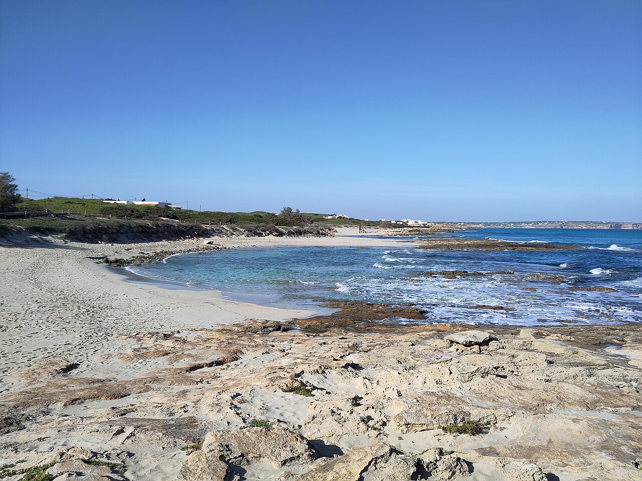 Een van de zandkommen van Ses Platgetes op Formentera, met turquoise water tussen de rotsplaten en duinen erachter