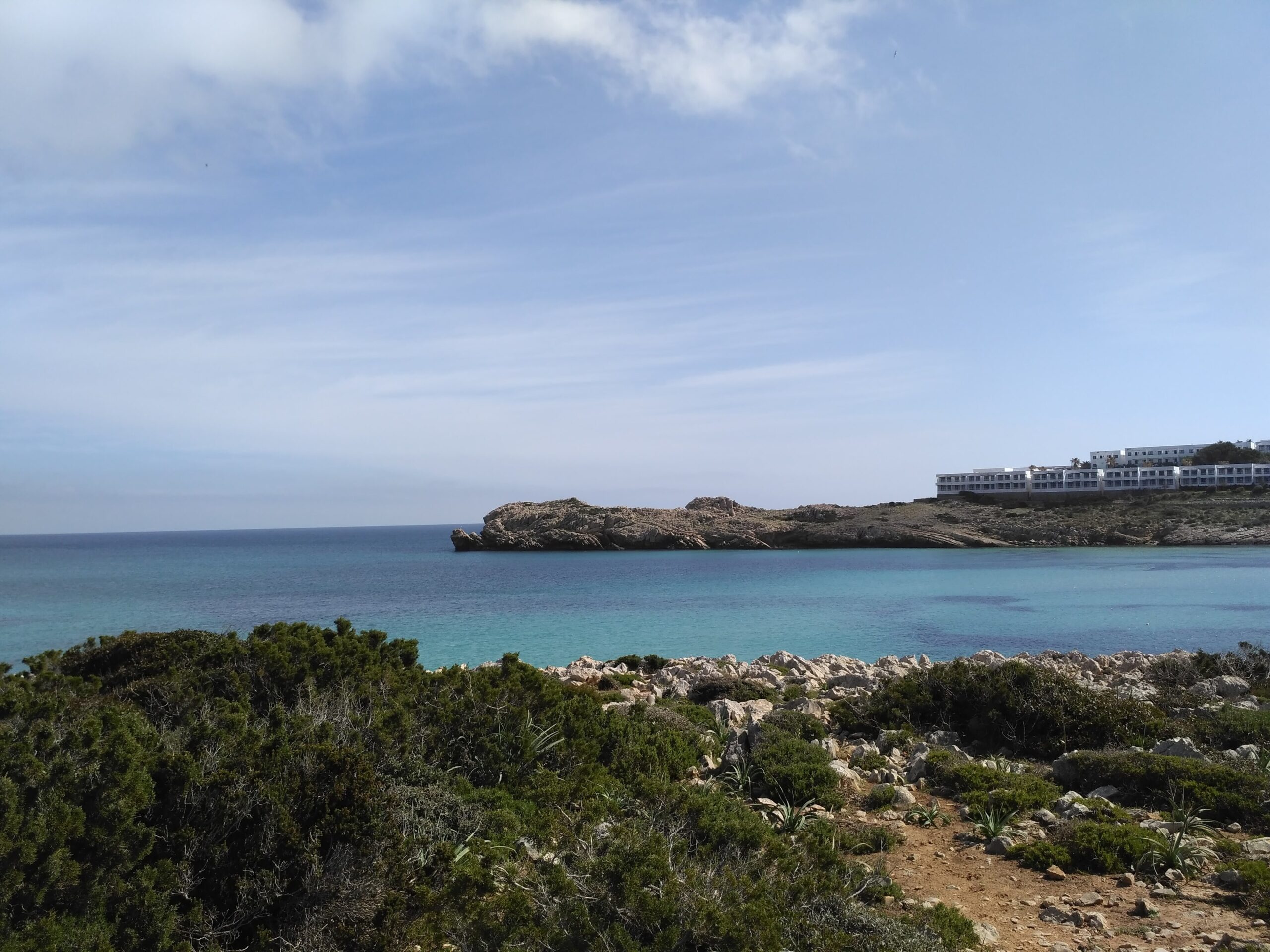 Son Parc Menorca: het duinstrand en de enige golfbaan van het eiland 1 Turquoise water van de baai van Son Parc met de rotskop en de witte appartementen erachter