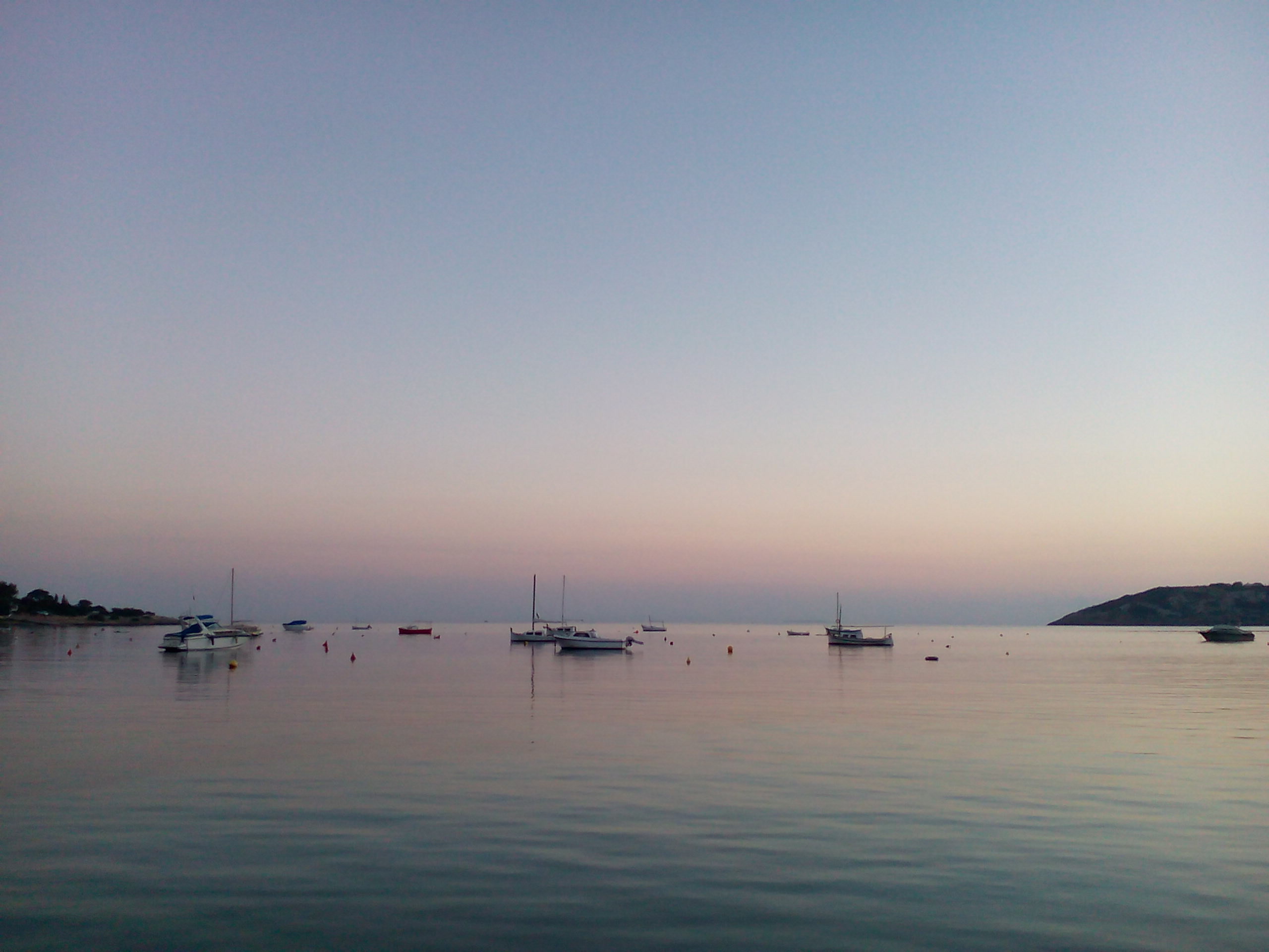 Spiegelglad water in de baai van Talamanca bij het eerste licht in december, met zeilboten en vissersbootjes voor anker en een roze gloed boven de horizon
