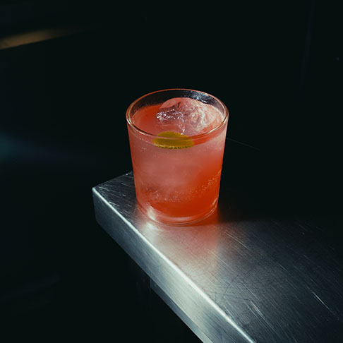 Roze cocktail met een takje kruid op de metalen bar van Terrae in Port de Pollença
