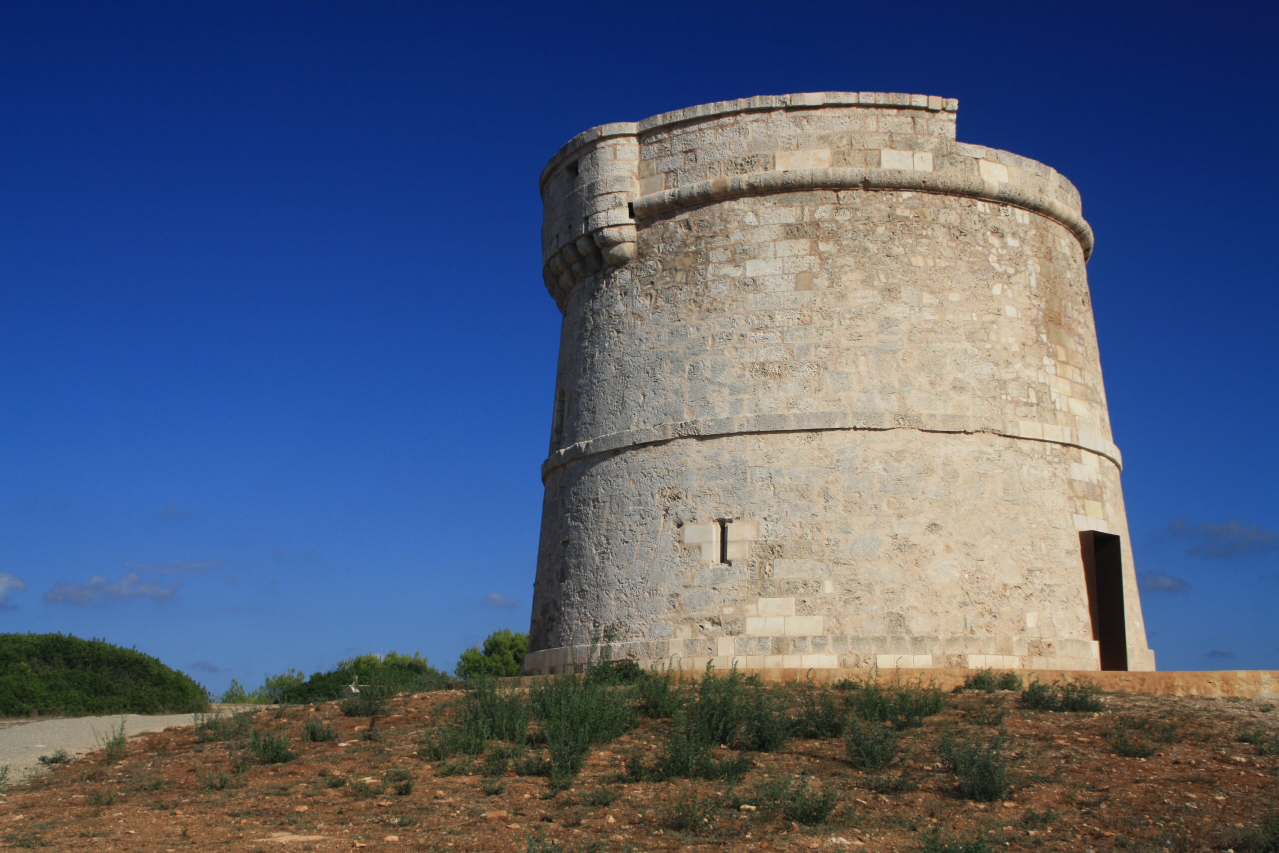 De ronde stenen Torre de Son Ganxo bij Punta Prima op Menorca tegen een diepblauwe lucht