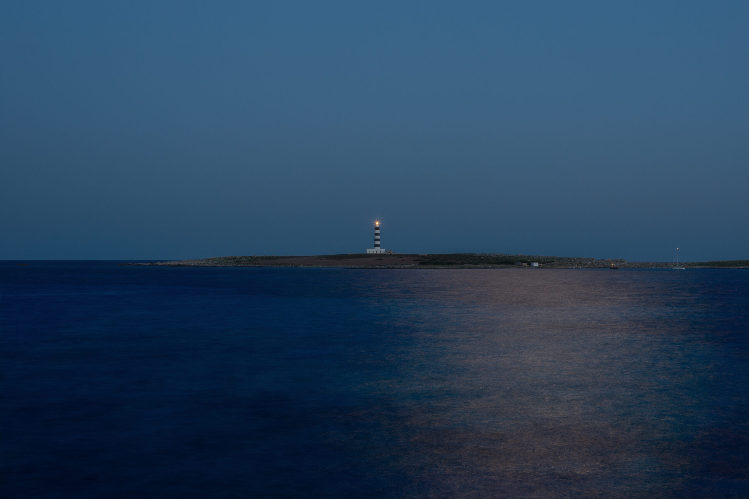 De vuurtoren van Illa de l'Aire flitst boven het donkerblauwe water tijdens het blauwe uur